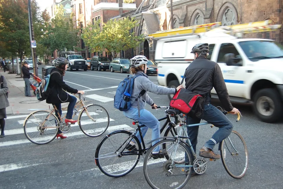 People on bike wearing helmets stopped at intersection waiting for passing cars in Philadelphia, Pennsylvania.